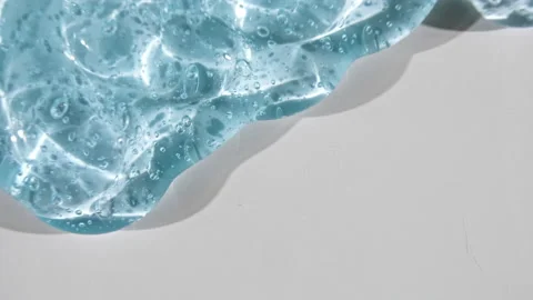 Transparent blue gel fluid with bubbles flowing down on a white surface. Macro Stock Footage 143186498