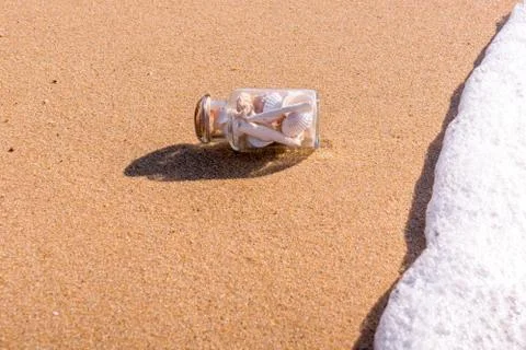 Transparent bottle with shells on the beach in the waves Foto stock