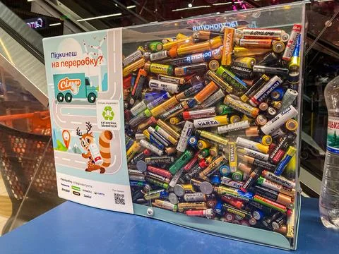 Transparent container holding assorted used batteries on a flat surface, next Stock Photos