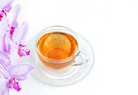 A transparent cup of aromatic tea and a pink orchid on a white background Stock Photos