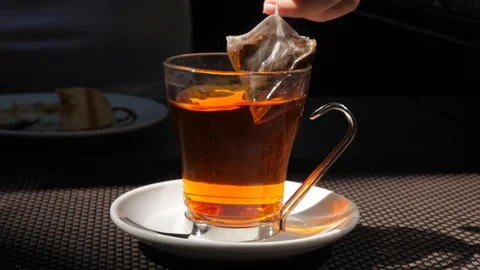Transparent cup with tea bag floating in hot water, woman take away it Stock Footage 103182687