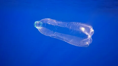 Transparent disposable plastic bottle sinks in blue water, from bottle come out Stock Footage 255111178