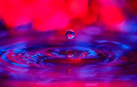 A transparent drop with a red-violet background falls into the water. Abstr.. Stock Photos