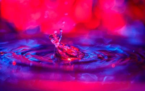 A transparent drop with a red-violet background falls into the water. Abstract Stock Photos