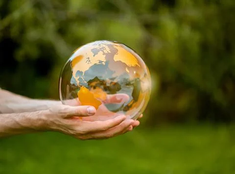 Transparent earth globe with golden yellow continents held in two hands. Stock Photos