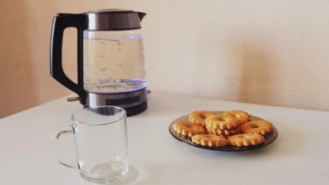 A transparent electric kettle with a blue backlight on a table with cookies.. Stock Footage 333473819