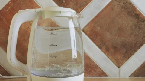 A transparent electric kettle on the table begins to boil Vidéo 318178548