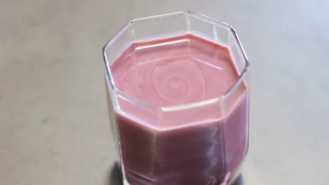 Transparent glass cup with milk on the table. Rotation of pink liquid in a glass Stock Footage 112939479