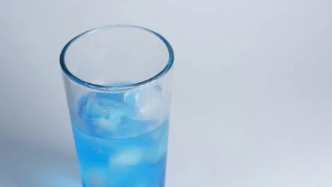 Transparent glass filled with ice cubes and blue soda Stock Footage 228874324