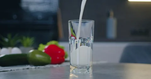 Transparent glass standing on kitchen table and is poured with fresh milk Stock Footage 148739387