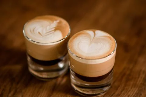 Transparent glasses of coffee drink with pattern on white foam on wooden table. Stock Photos