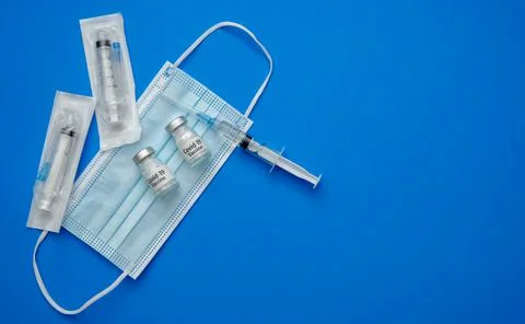 Transparent medical ampoules, syringe and protective mask on a light blue bac Stock Photos