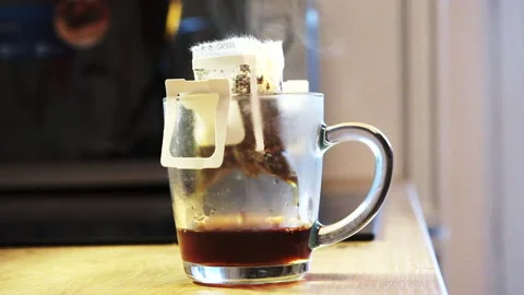 A transparent mug with fresh made coffee in a drip bag with drops dripping Stock Footage 288454655