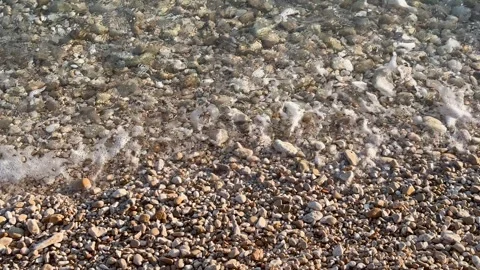 Transparent ocean waves retreating over pebbled beach revealing wet stones Stock Footage 317253564
