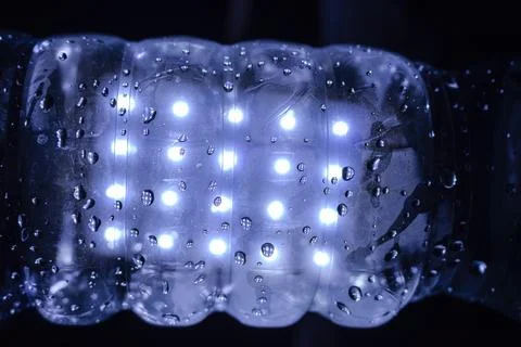 A transparent plastic bottle with glowing lights and water droplets Stockfoto's