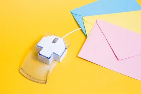 Transparent plastic computer mouse and paper colored envelopes on a yellow ba Stock Photos