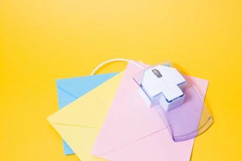 Transparent plastic computer mouse and paper colored envelopes on a yellow ba Stock Photos