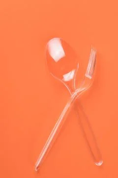 Transparent plastic fork and spoon on orange background Stock-Fotos