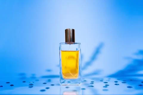 Transparent rectangular bottle of golden perfume on blue background with shad Stock Photos