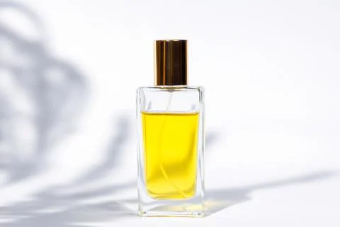 Transparent rectangular bottle of golden perfume on white background with sun 스톡 사진