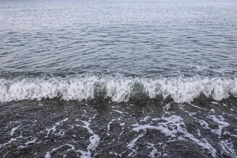 Transparent sea wave on the shore of a pebble beach on a sunny day Stock Photos