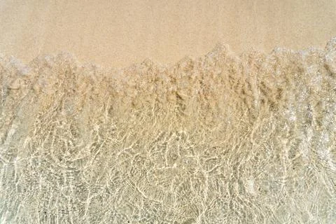 A transparent small wave rolls onto a sandy shore. Stock Photos