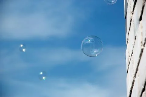 Transparent soap bubble on blue sky with clouds and white brick wall backgrou Stock Photos