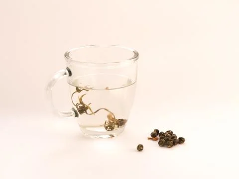 A transparent tea mug filled with tea with jasmine tea balls next to it. Stock Photos