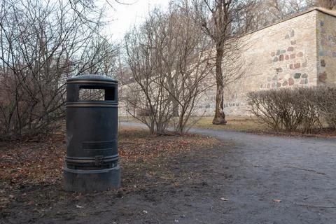 Trash bin placed in a park landscape with leafless trees and open space. Stock Photos
