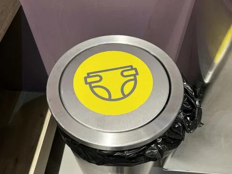Trash bin with yellow lid displaying diaper icon Stock Photos