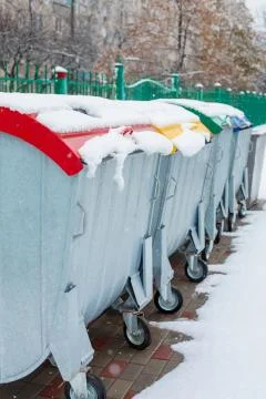 Trash bins for sorting garbage are standing on the street covered with snow. Stock Photos