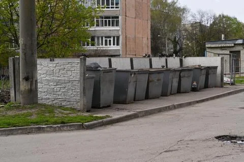 Trash container row stands along residential street near apartment building. Photos