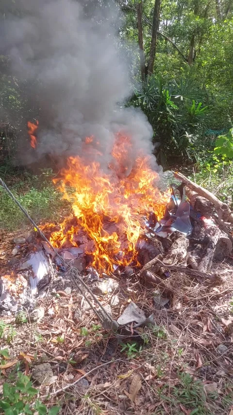 Trash pile on fire in open green area – aerial perspective Stock Footage 312494892
