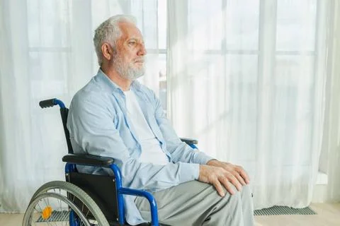 Trauriger älterer Mann sitzt im Rollstuhl und schaut aus dem Fenster im Al.. Stock Photos