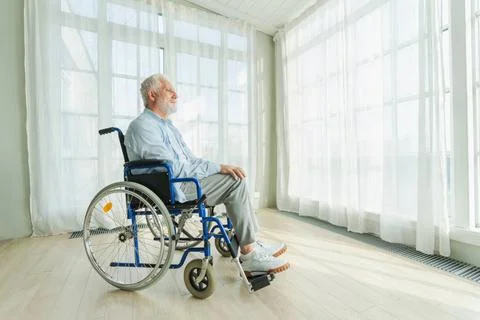 Trauriger älterer Mann sitzt im Rollstuhl und schaut aus dem Fenster im Al.. Stock Photos
