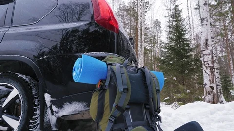 A travel backpack with a mat stands next to the crossover car. Stock-Footage 104465703