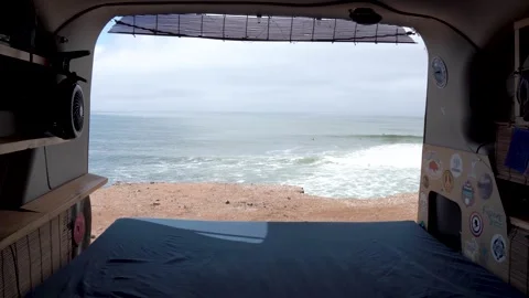 Travel van with back door open to ocean view with surfers in the distance, Stock Footage 241302141
