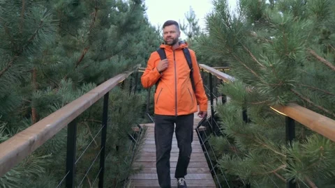 Traveler with backpack and orange jacket walking along wooden path Video stock 282455809