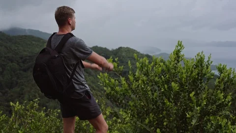 A traveler with a backpack on his back, stands on the top of a hill and shoots a Stock Footage 107328210