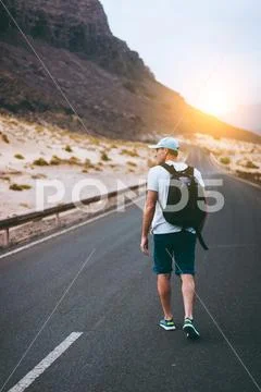 Traveler with backpack walks in the center of an epic winding road. Huge Stock Photos