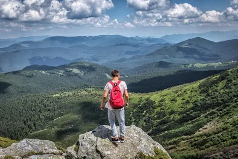 Traveler man with red backpack in mountains. Summer view forest, clouds Stock Photos
