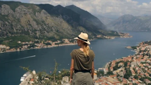 Traveler pulls her hands up standing on a cliff overlooking the mountain bay Video stock 92138543