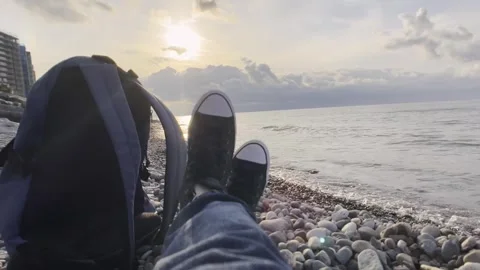 Traveler throws backpack, relaxes on seashore in classic sneakers against sunset Stock Footage 291783558