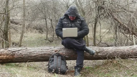 A traveler is typing something on a laptop while sitting on a lying pine tre Vídeos de archivo 175061307