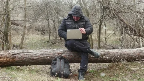 A traveler is typing something on a laptop while sitting on a lying pine tre Vídeos de archivo 175061549