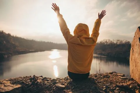 Traveler woman looking at sunset near lake with raised hands Stock Photos
