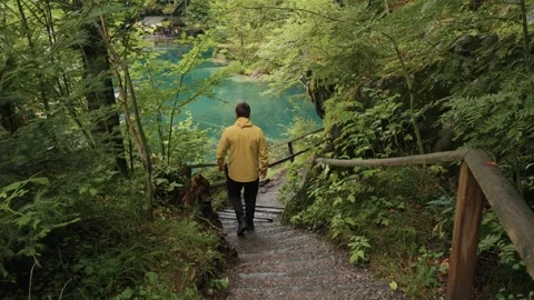 Traveler in yellow jacket walking down wooden stairs at Blausee Switzerland lake Stock Footage 320103503