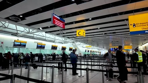 Travelers queuing at check in desks inside Heathrow Terminal 4 airport with Stock Footage 334973537