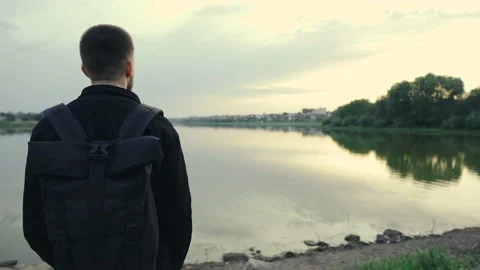 Traveling man with backpack standing looking at beautiful sunset near the river Stock Footage 132947941