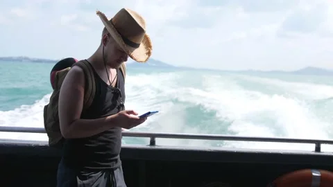 Traveling man in hat with backpack using mobile phone while cruising on boat Stock Footage 195974724